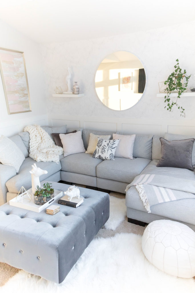 Light and bright kid-friendly living room with cozy gray sectional, marble wallpaper, pink abstract art and velvet ottoman