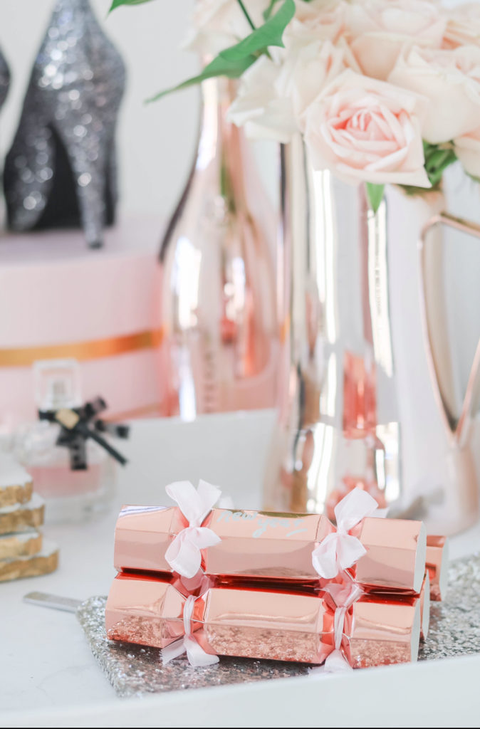 New Year's Eve styled vanity with rose gold crackers, sparkly heels, sparkling rosé , perfume and fresh roses