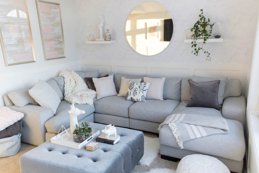 Light and bright kid-friendly living room with comfortable sectional, marble wallpaper, oversized mirror and velvet ottoman