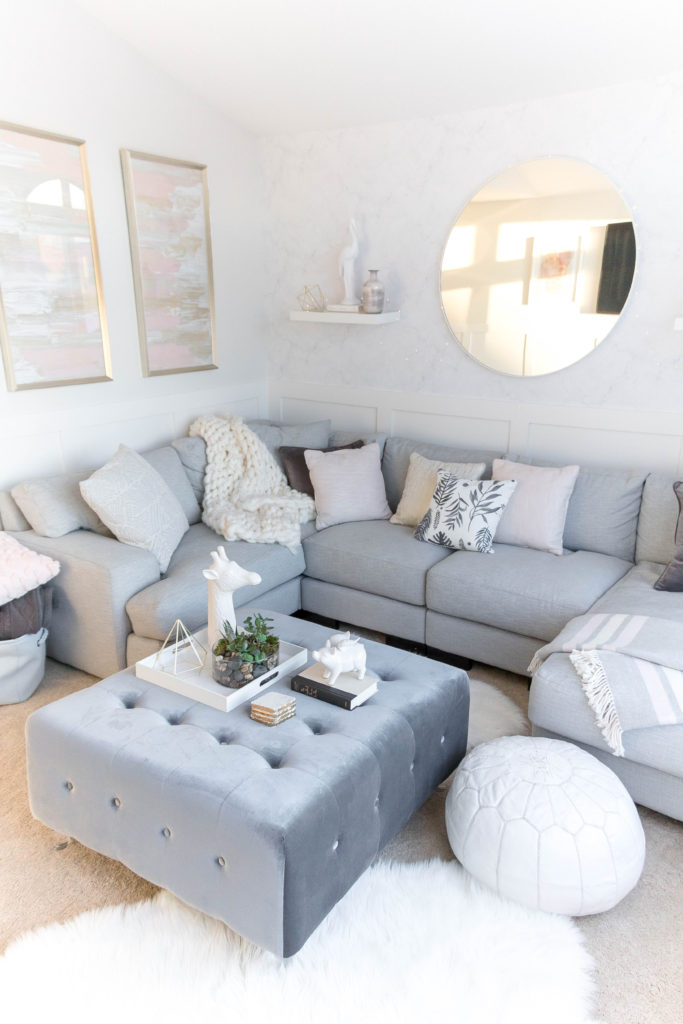 Light and bright kid-friendly living room with gray, white, pink and gold tones. Velvet ottoman. Moroccan pouf. Gray sectional. 