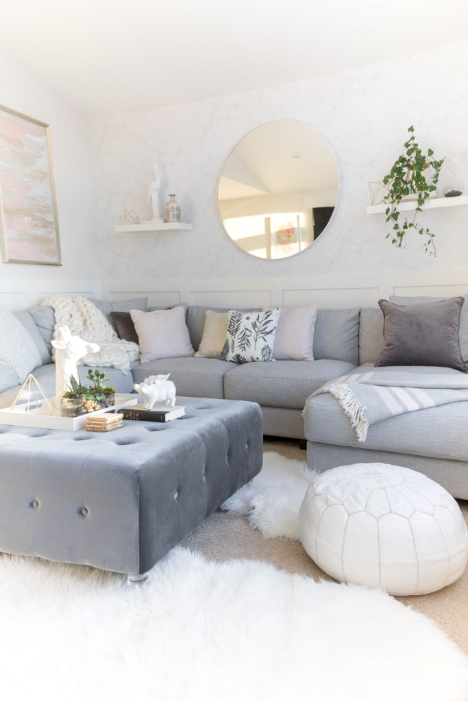 Light and bright kid-friendly living room with cozy gray sectional and velvet ottoman. Soft living room furnishings in white, gray, gold and pink.