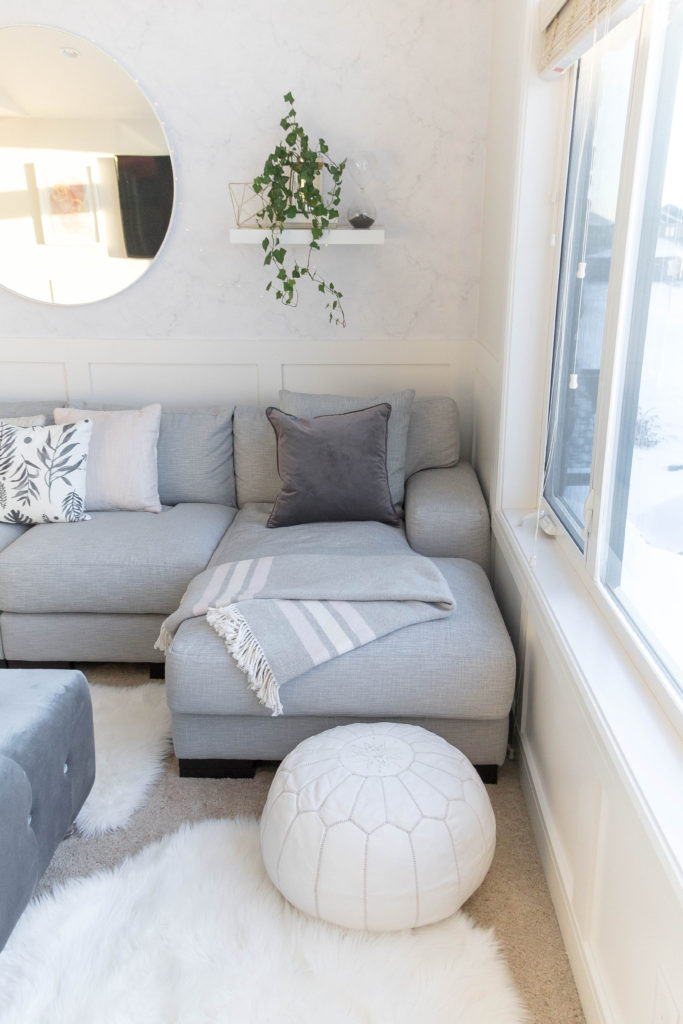 Light and bright kid-friendly living room with comfortable sectional, white faux fur rug, moroccan pouf and velvet ottoman