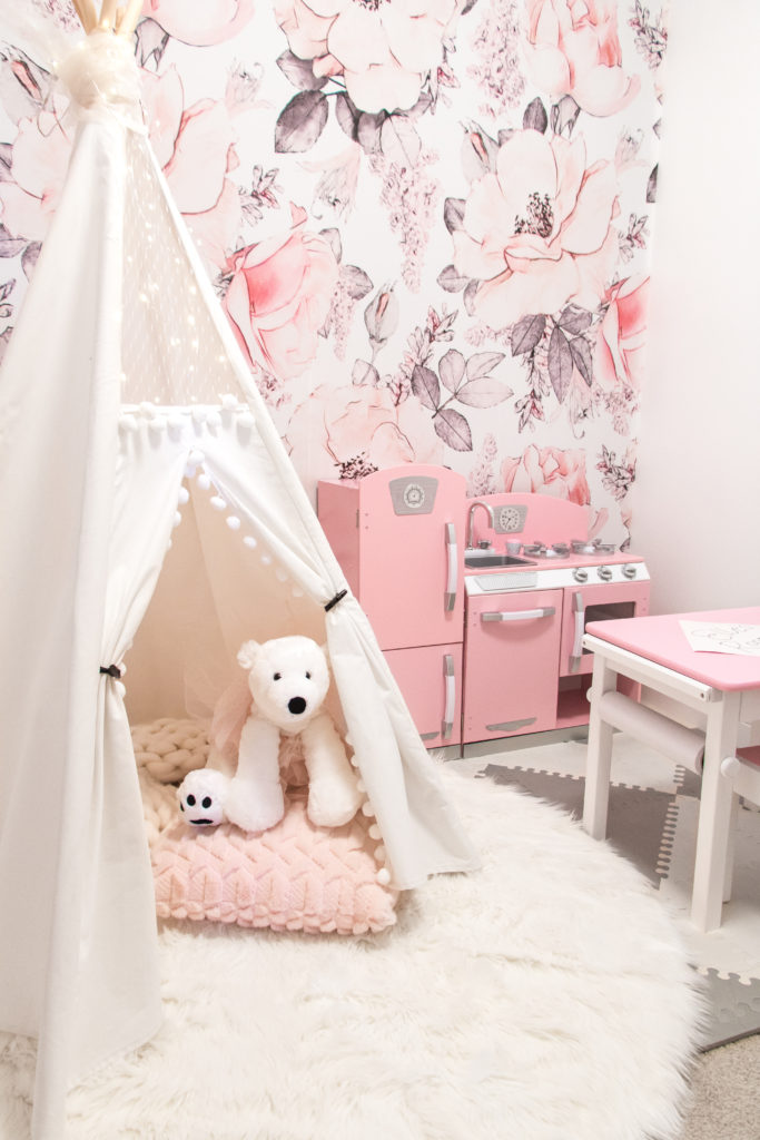 Glamorous pink playroom with rose wallpaper, white kids teepee, pink play kitchen and pink desk. Glamorous and girly kids toy room. Toy room decor ideas. 