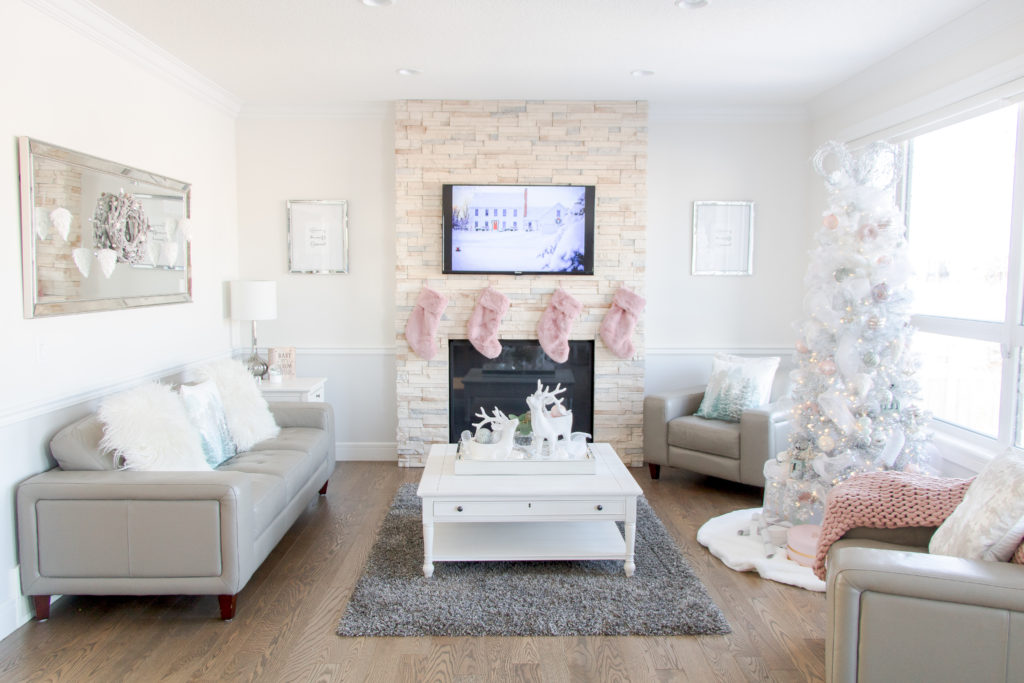 Living room with pastel Christmas decor and white ombre Christmas tree, pink fuzzy stockings and Urban Barn coffee table decor