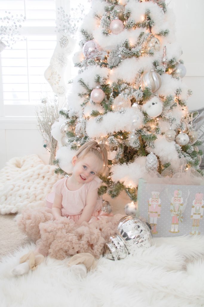 My toddler daughter in a pink tutu in front of our white and pastel fluffy Christmas tree