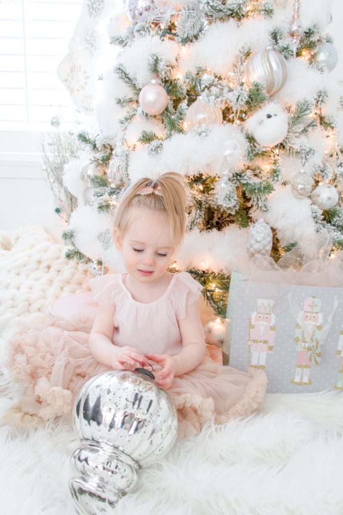 My toddler daughter in a pink tutu in front of our white and pastel fluffy Christmas tree with a mercury glass oversized ornament