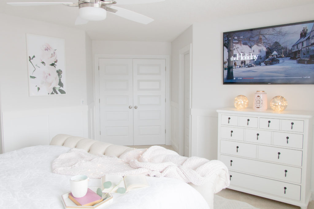 Light and bright white luxurious master bedroom with white furniture, wainscoting and floral art