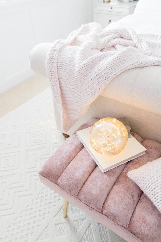 Pink velvet bedroom bench, neutral rug, chunky knit blanket and white luxurious master bedroom details 