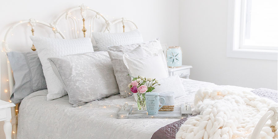 Light and airy guest bedroom with white and gray bedding, a wrought iron bed frame and vintage inspired furniture on Chandeliers and Champagne