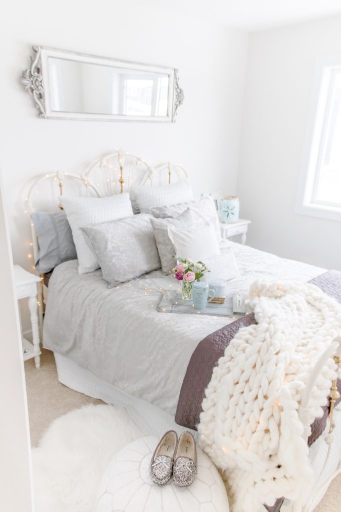 A vintage-inspired airy guest bedroom decorated in white and gray tones with plush bedding