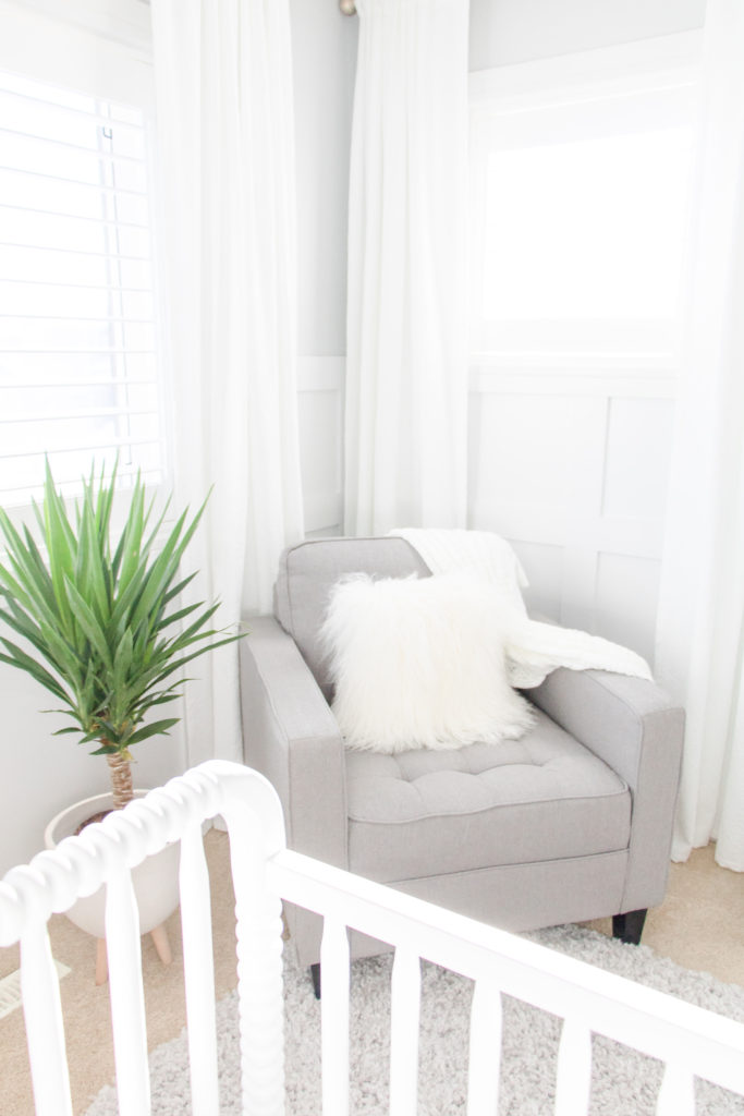 White and grey gender-neutral nursery with gray feeding chair, white drapes, white wainscoting and white shutters