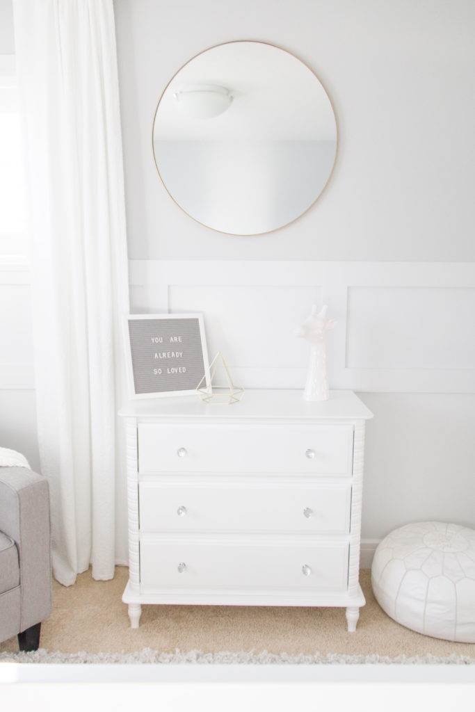 Modern gender-neutral nursery: white dresser with gold tone circular mirror. Grey gender-neutral nursery inspiration.