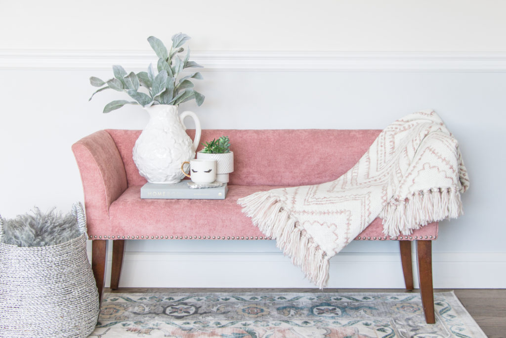 Blush pink velvet bench styled with a vase, throw blanket and pastel area rug: Pastel Living Room Decor