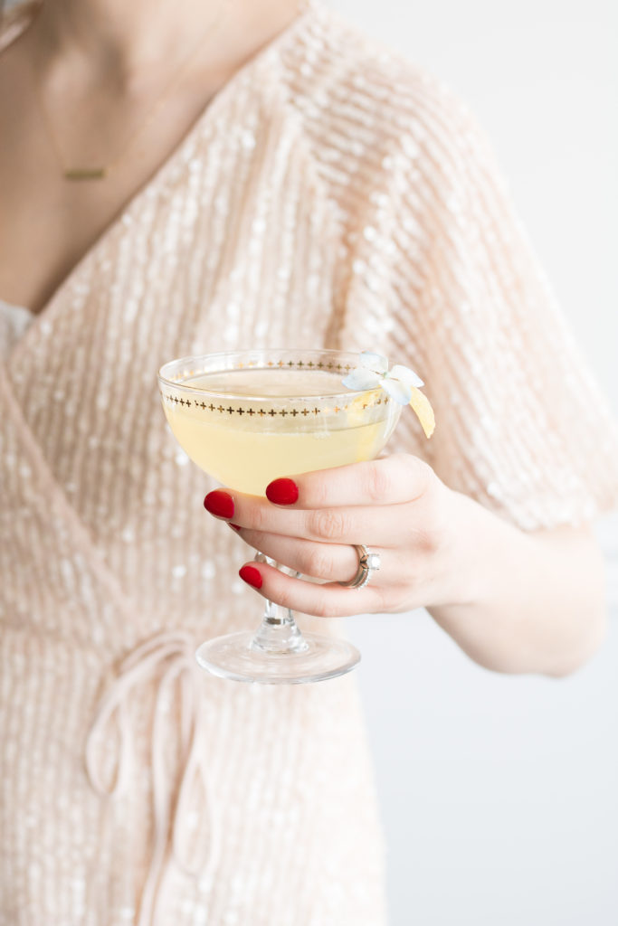 Woman in sequinned party dress with red nails holding Elderflower French 75 cocktail