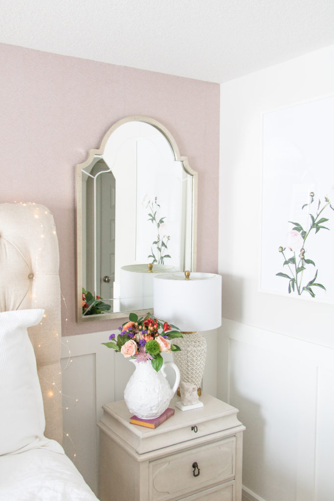 Luxurious master bedroom with arched silver leaf mirror, neutral bedside tables, pink wallpaper, white lamp and neutral decor
