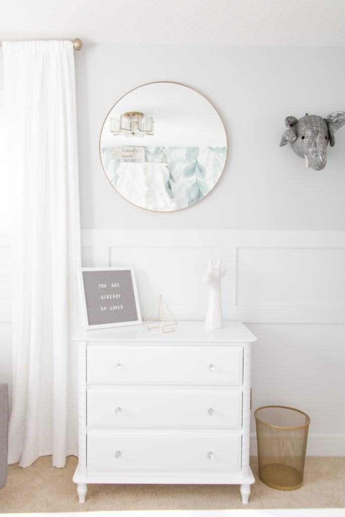View of white nursery dresser topped with a letter board and giraffe head decor