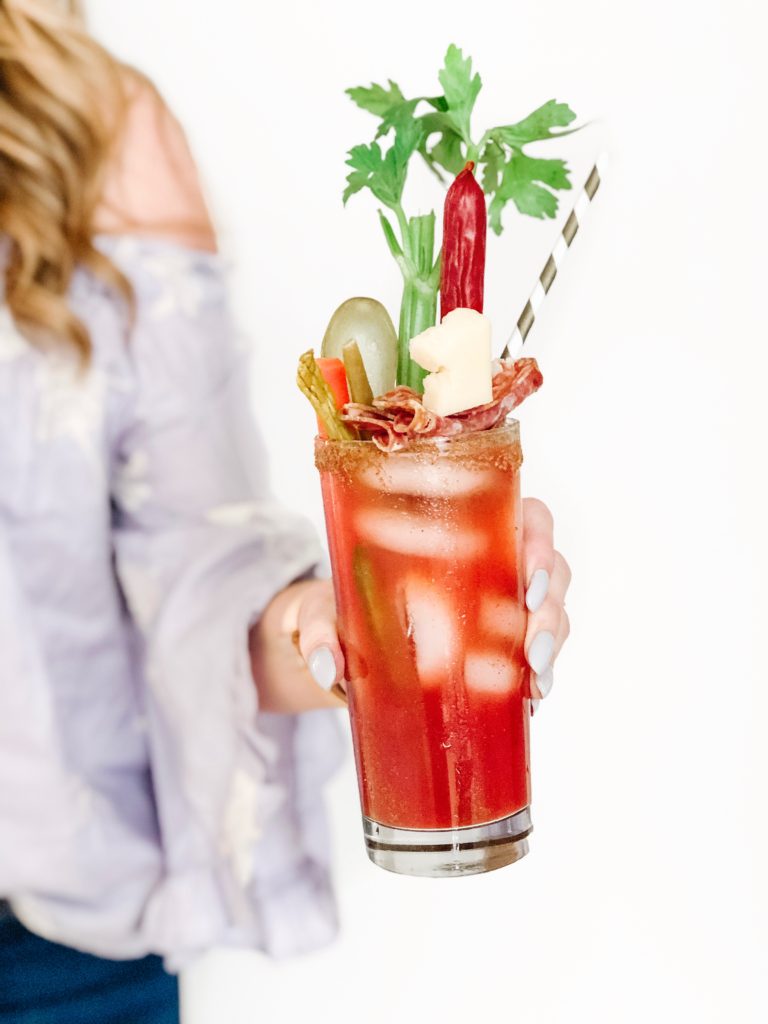 Close-up of Charcuterie Gin Caesar and it's fun toppings held by blogger Holly Hunka