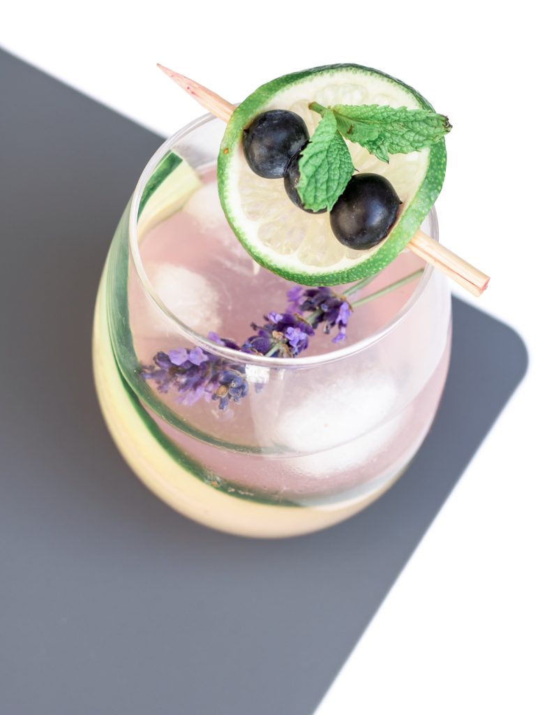 Closeup shot of pink cocktail with cucumber, mint, lavender and blueberries