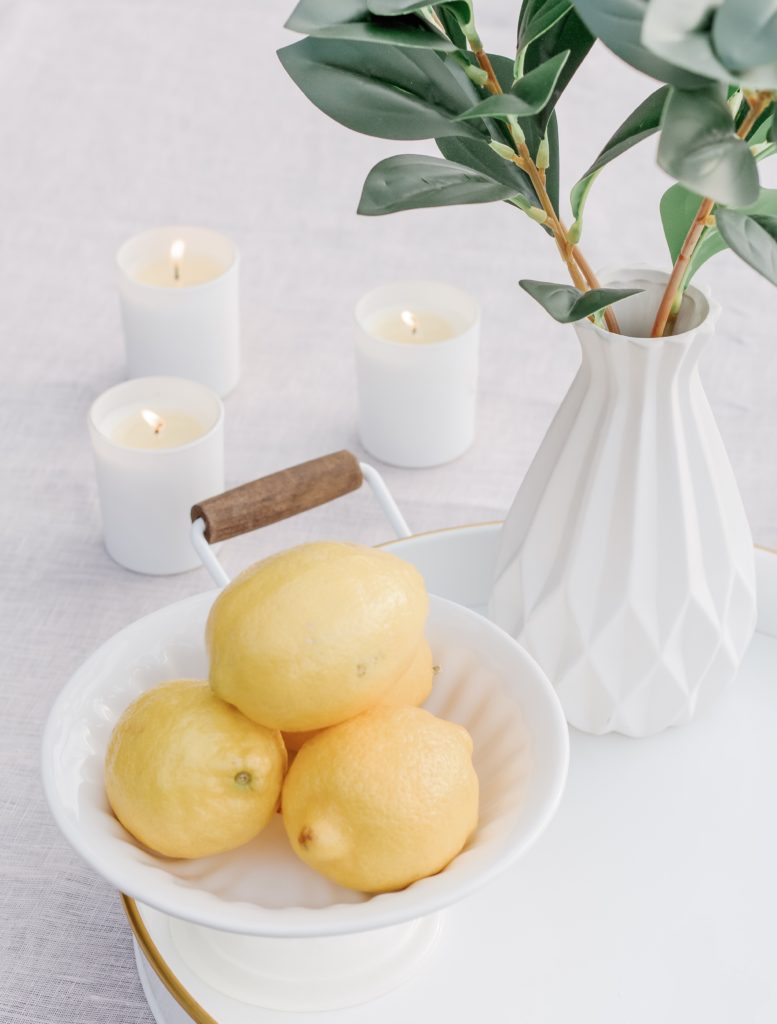 Closeup photographs of lemons in a bowl on a white tray with greenery and three candles