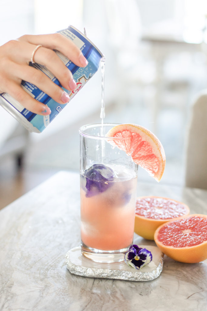 Woman pouring club soda into Layered Grapefruit and Rose Vodka Soda