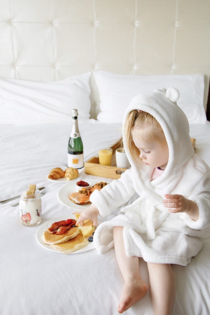 Toddler enjoying breakfast in bed room service at Sheraton Cavalier Calgary Hotel