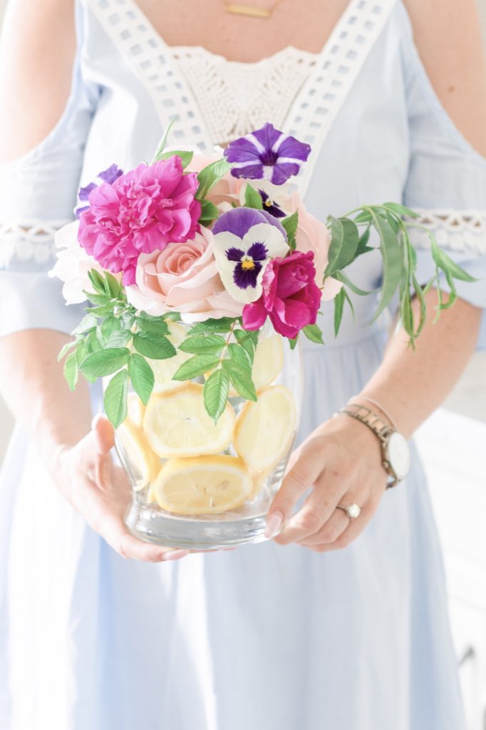Closeup of woman in blue dress holding a vase with floating lemons and fresh flowers
