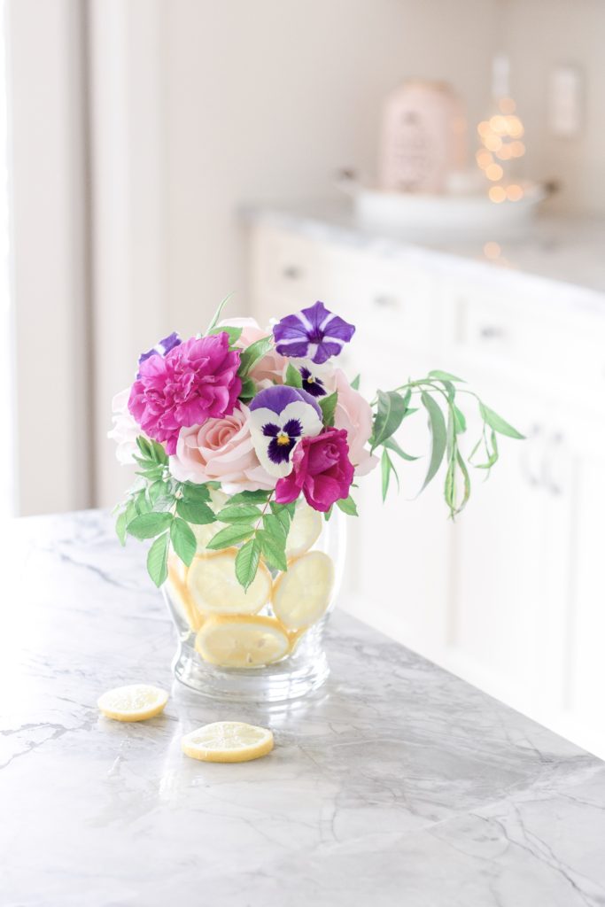Floating lemon vase with flowers sitting on top of a gray and white granite kitchen countertop