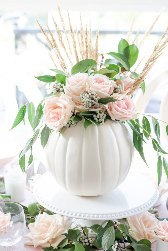 Closeup of white DIY pumpkin vase with greenery, pink roses and grass