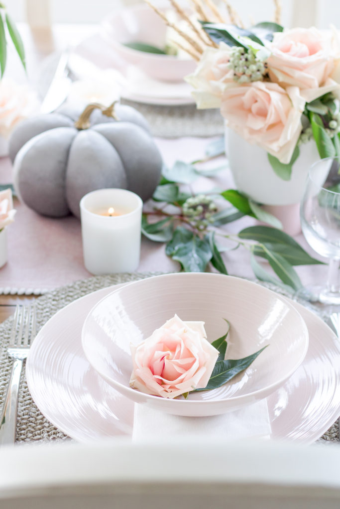 Closeup of blush pink plates and greenery as part of charming fall table setting
