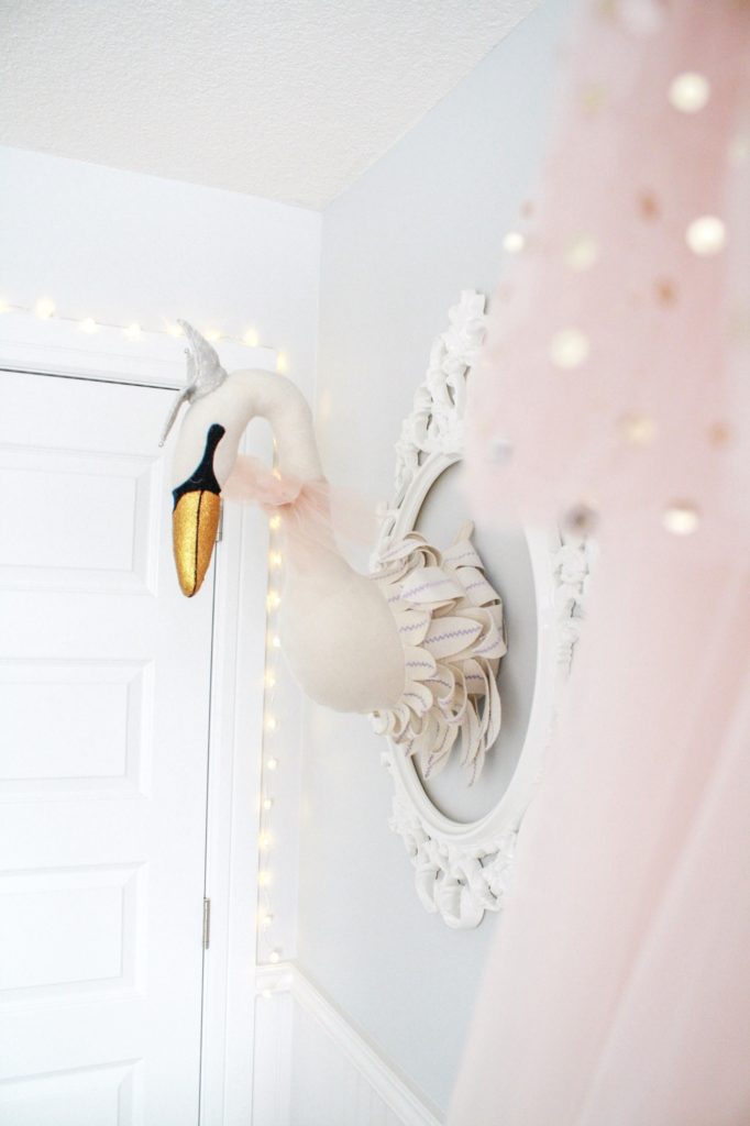 Swan nursery decor: faux taxidermy swan head with gold beak, twinkle lights and pink tulle crib canopy