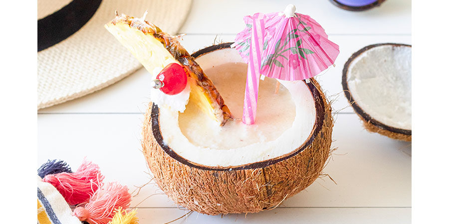 Piña Colada cocktail in a coconut with pineapple wedge and cherry