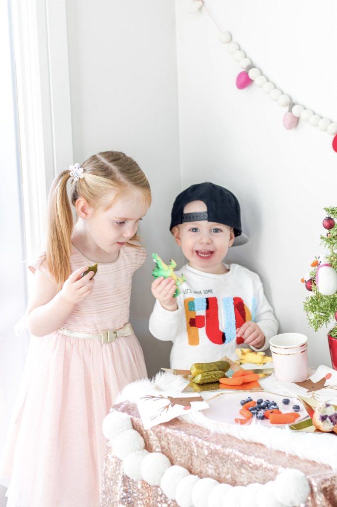Kids enjoying Christmas themed snacked table with pompom garland: Kids’ Christmas Party Table